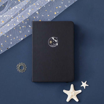 Tsuki deep black Playful Orca limited edition notebook at an angle with starfish and free sunshine gift on dark blue background